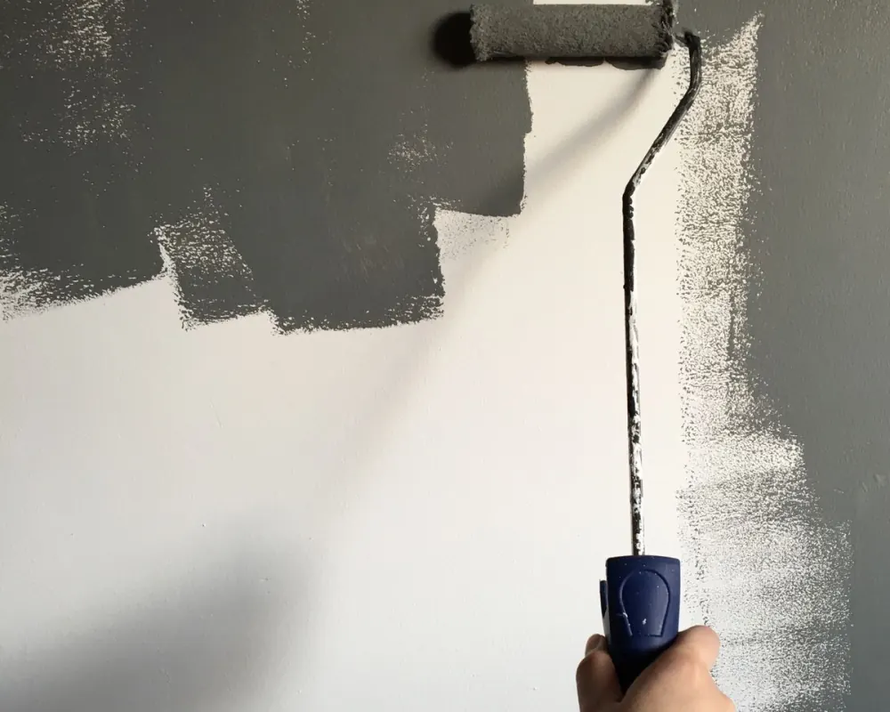 A hand carefully applying gray paint to an interior wall with a roller — illustrative stock photo